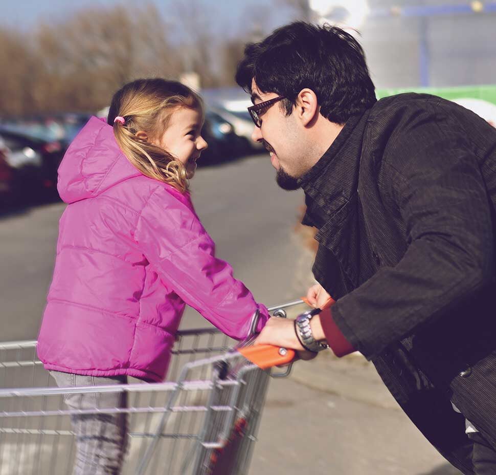 A man pushes a young girl in a shopping cart