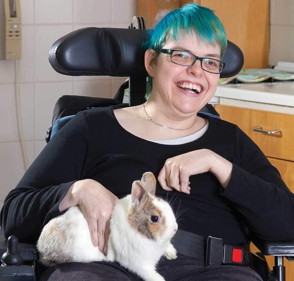 A woman in a wheelchair smiles. She has a rabbit in her lap