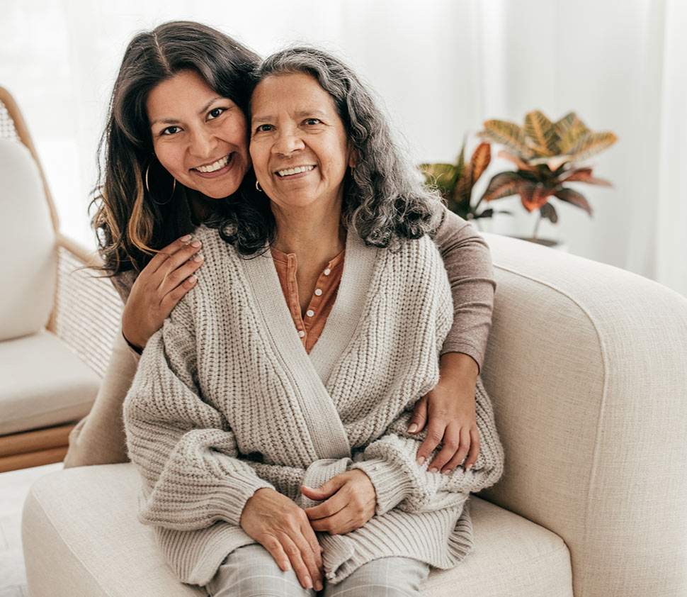 An older woman smiles as her personal care attendant gives her a hug.