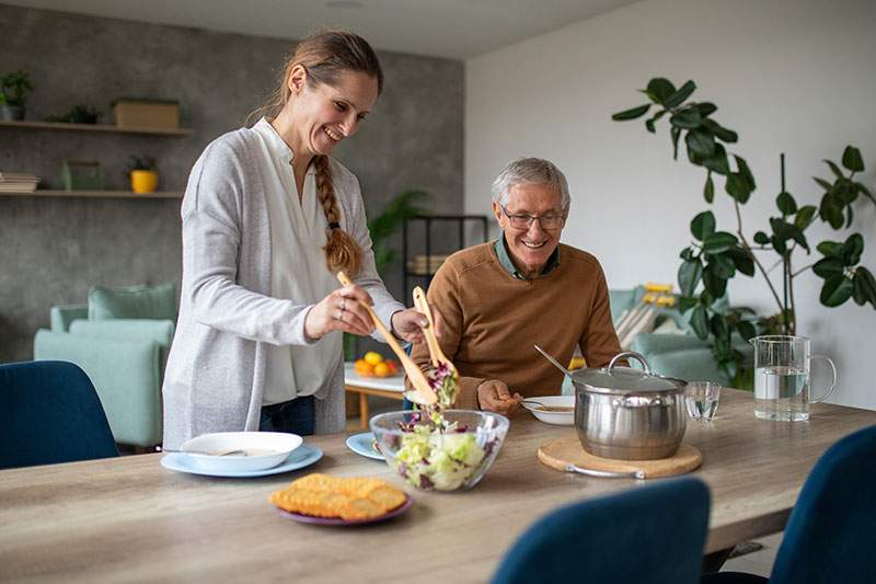 An in-home caregiver serves lunch to an older man.