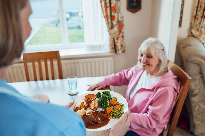 A personal care assistant in North Brunswick serves a meal to a senior client providing senior home care.