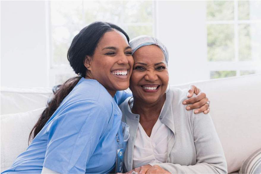 A caregiver hugging an elderly woman in a brightly-lit room