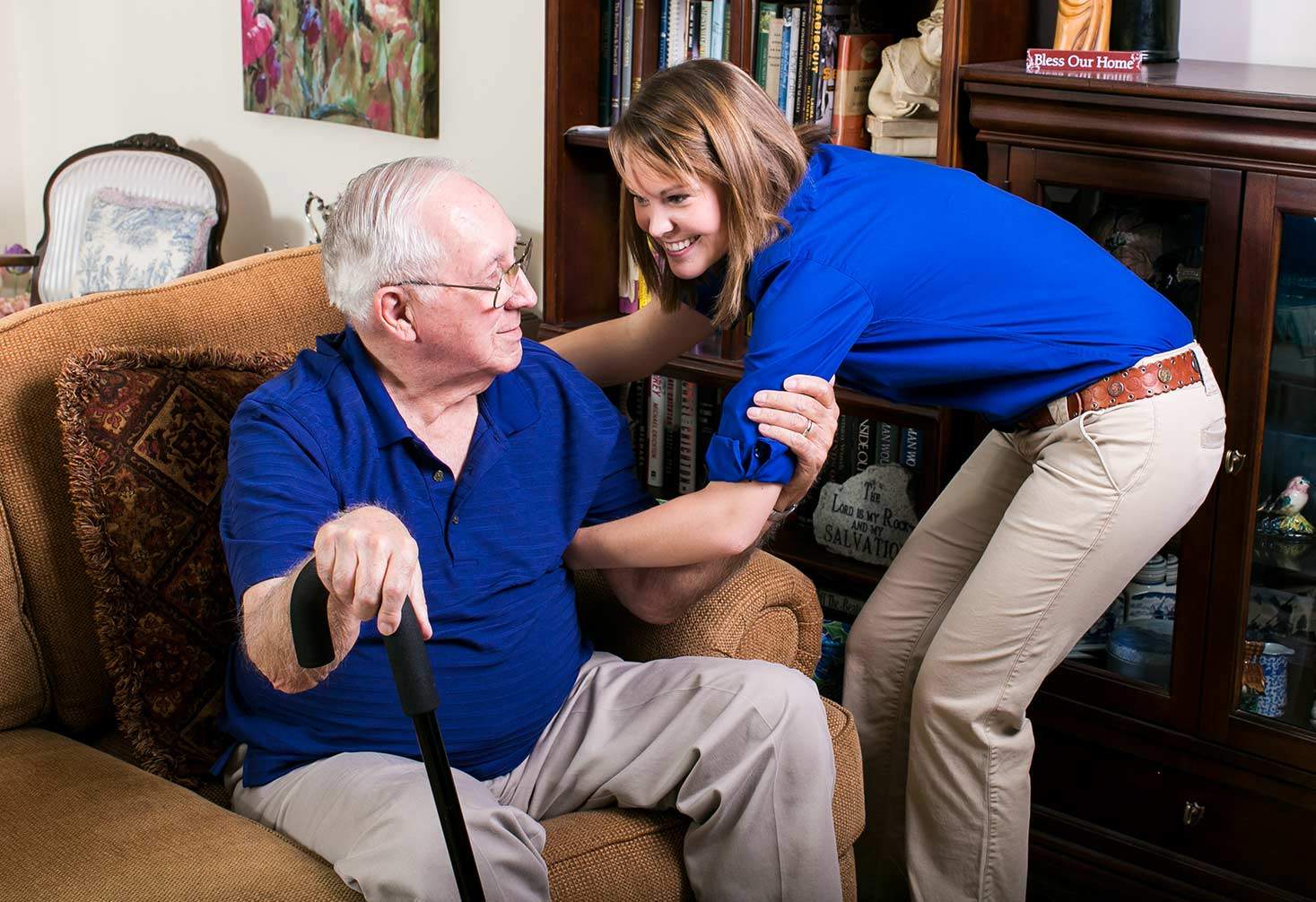 A caregiver supports a client in a chair who is holding a cane