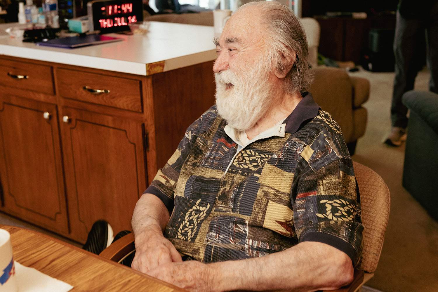 An elderly man laughs while sitting at a dining room table