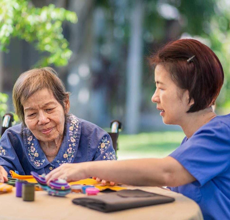 Older woman with caretaker crafting outside smiling