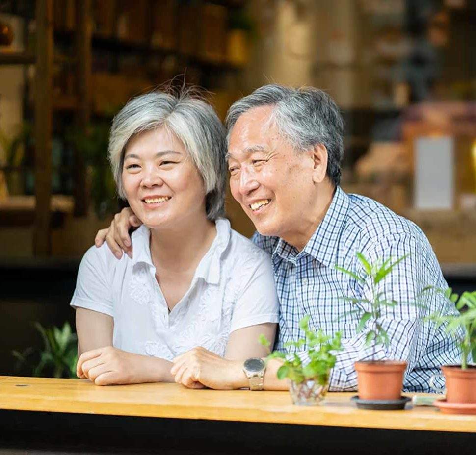 Older asain couple looking out the window and smiling together at a cafe