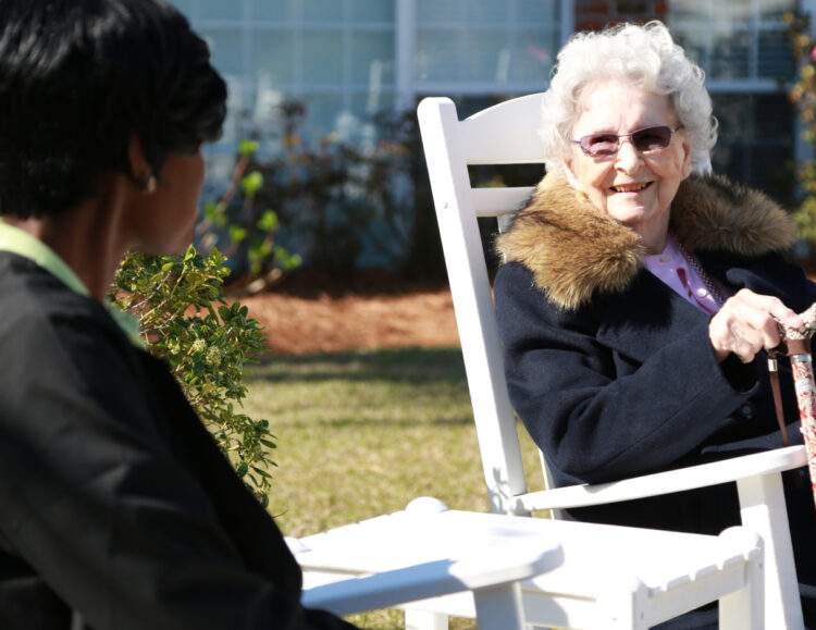 Ms. Schofield and her caregiver Cherise sit in rocking chairs outside and talk