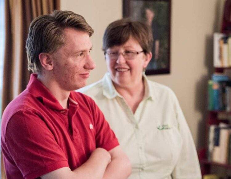 A man with disabilities stands in his living room with his caregiver