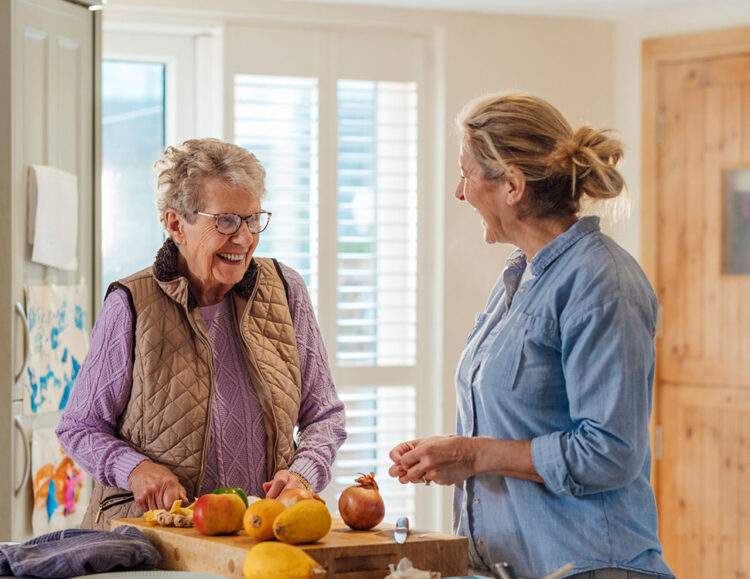 A personal care assistant helps a senior client prepare a meal.