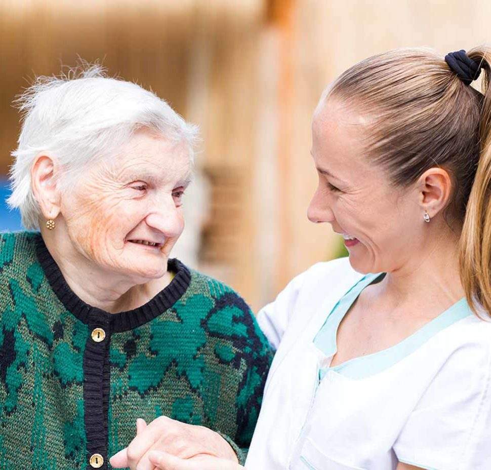 Caretaker and older woman laughing while walking outside together