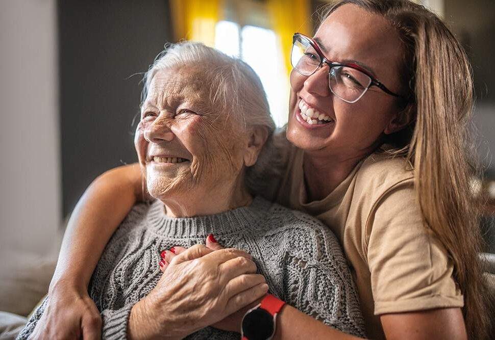 An in-home caregiver laughs with the older woman in her care.