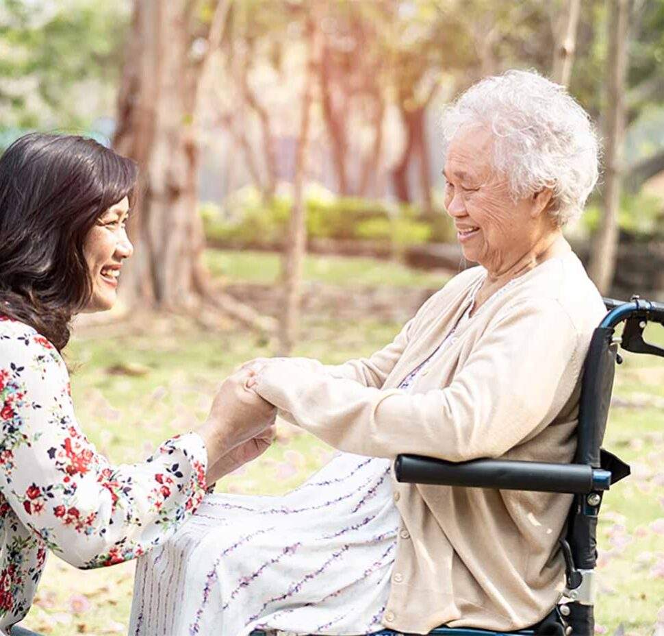 A woman kneels next to a senior in a wheelchair