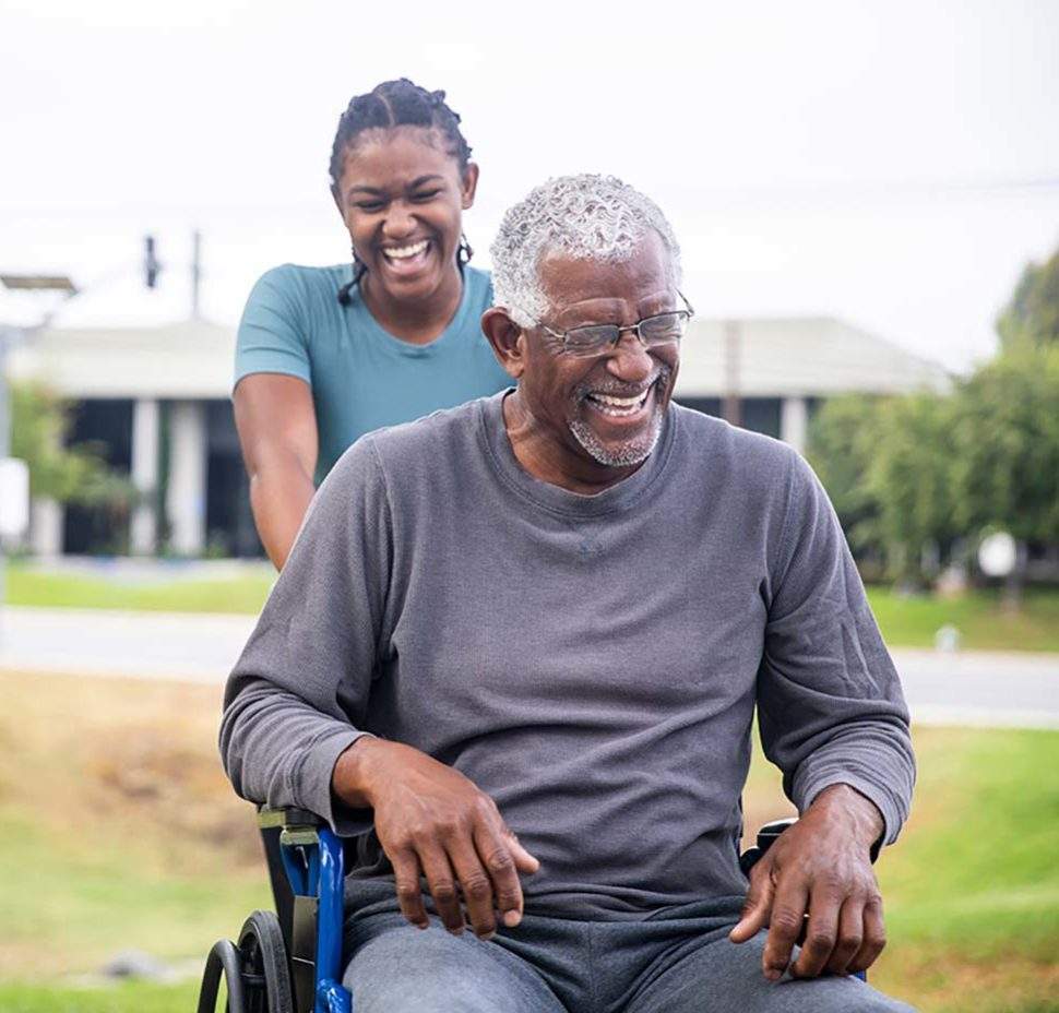 Woman pushing man in wheelchair outside while laughing