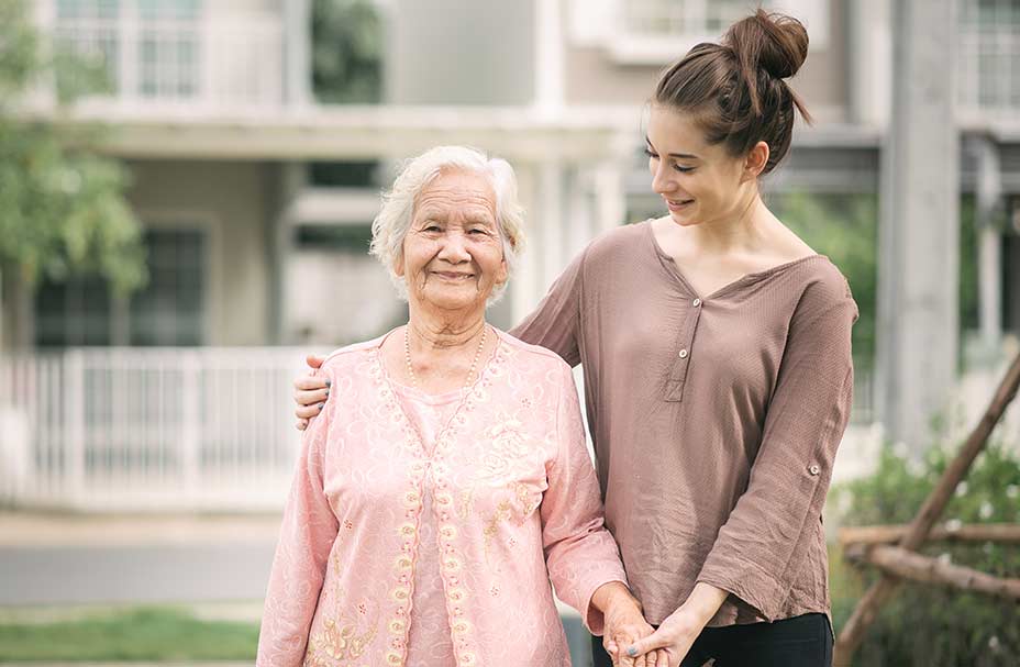 A caregiver walks with a senior and holds her hand