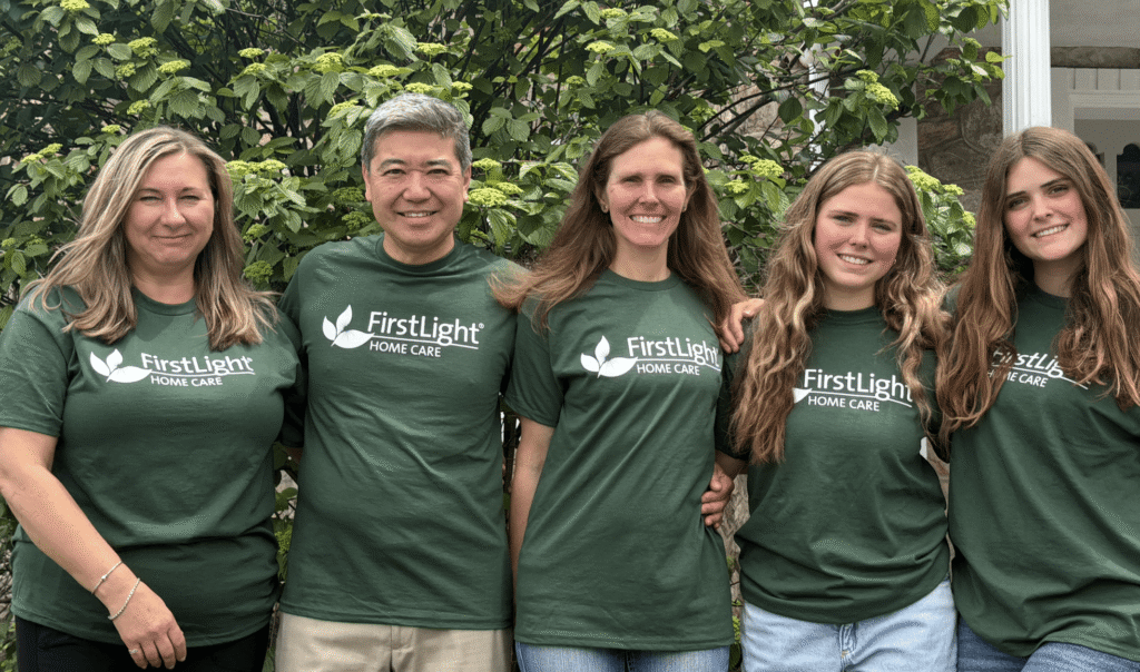 Team members of FirstLight Home Care of Northern Allentown standing together in branded green t-shirts, smiling outdoors.