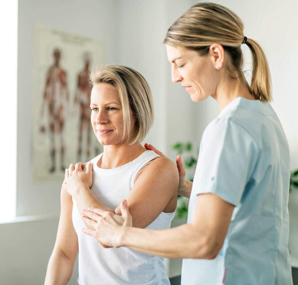 A women stretches as part of her physical therapy routine, while a caregiver watches