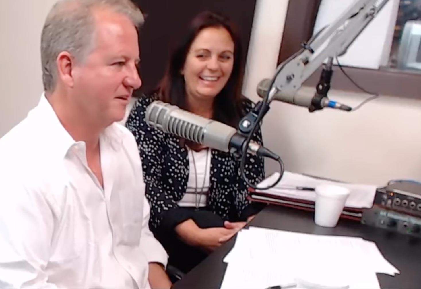 Chris and Jamie sit at a microphone while recording the radio TV show