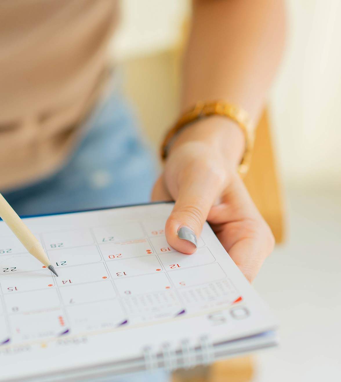 A woman holds a pencil above a planner that shows the days of the month