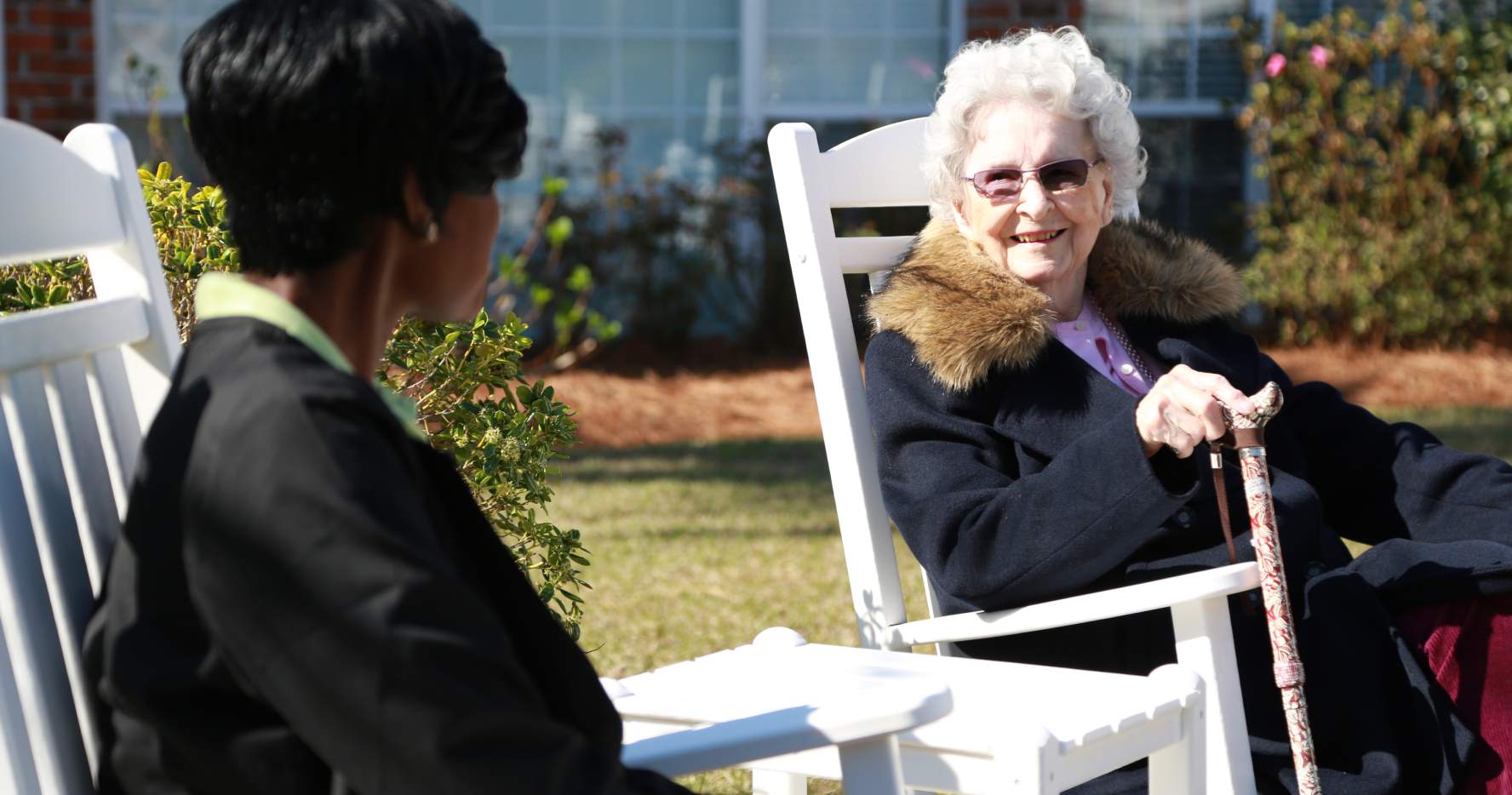Ms. Schofield and her caregiver Cherise sit in rocking chairs outside and talk