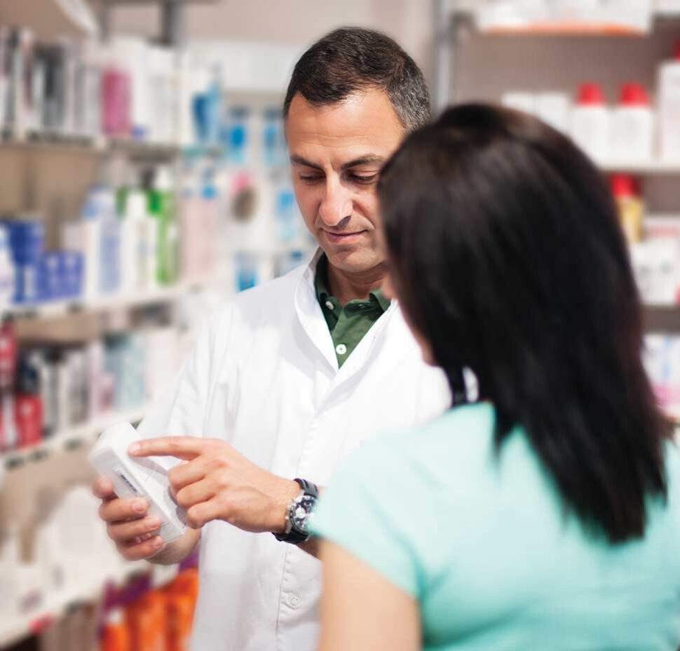 A pharmacist shows a pill bottle to a caregiver