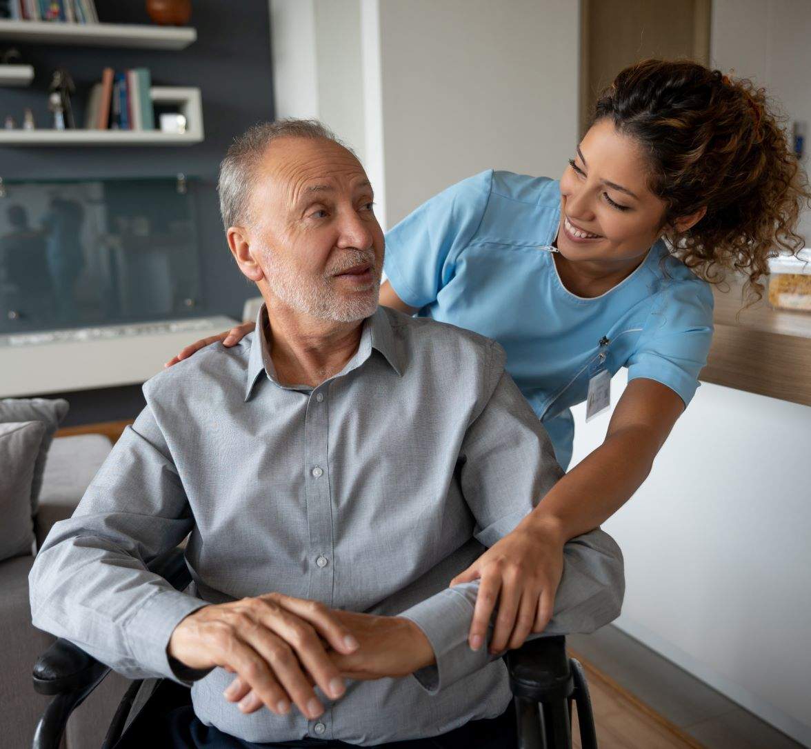 A caregiver leans over the shoulder of a sitting elderly man