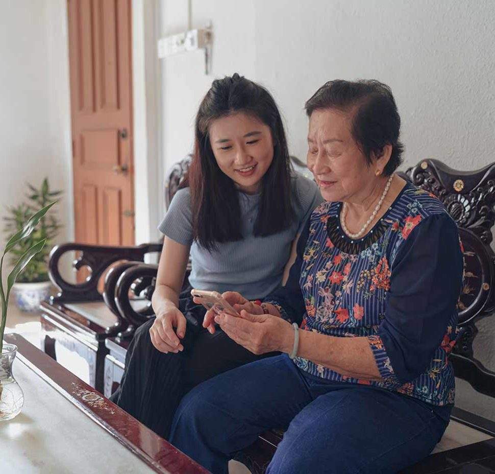 Older asain woman smiling at phone with female caretaker