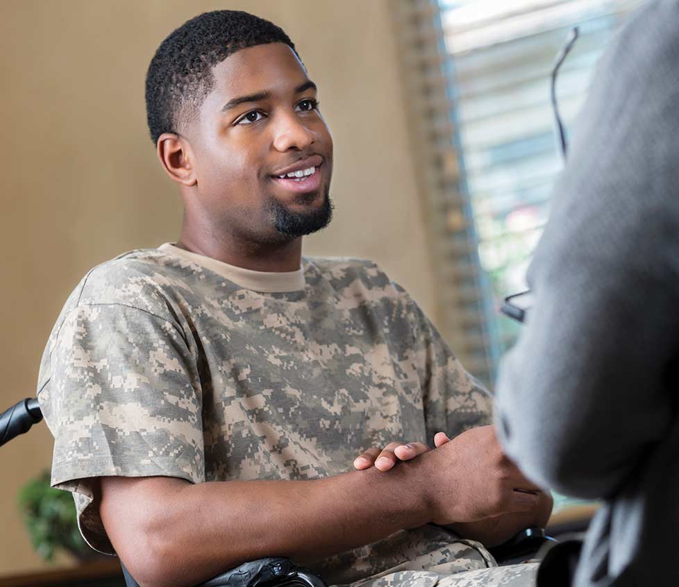 A young black man in a wheelchair speaks with a caregiver