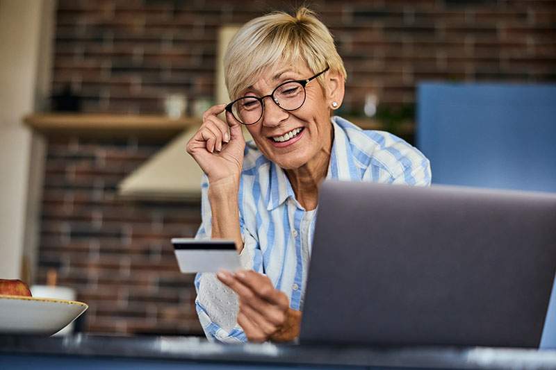 older woman holding a discount card and by a laptop