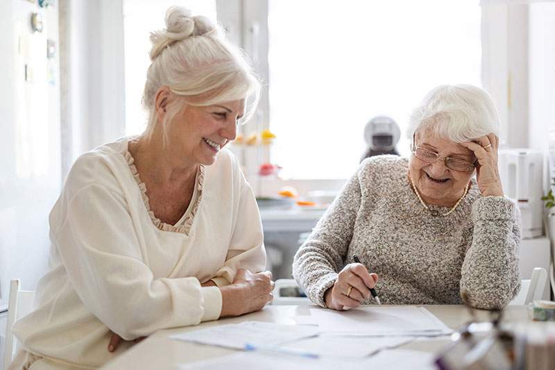Two elderly women seated at a table, reviewing papers