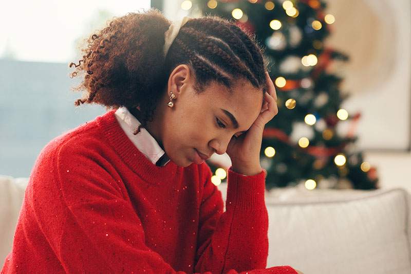 A woman in a red sweater sits on a couch, resting her head in her hands.
