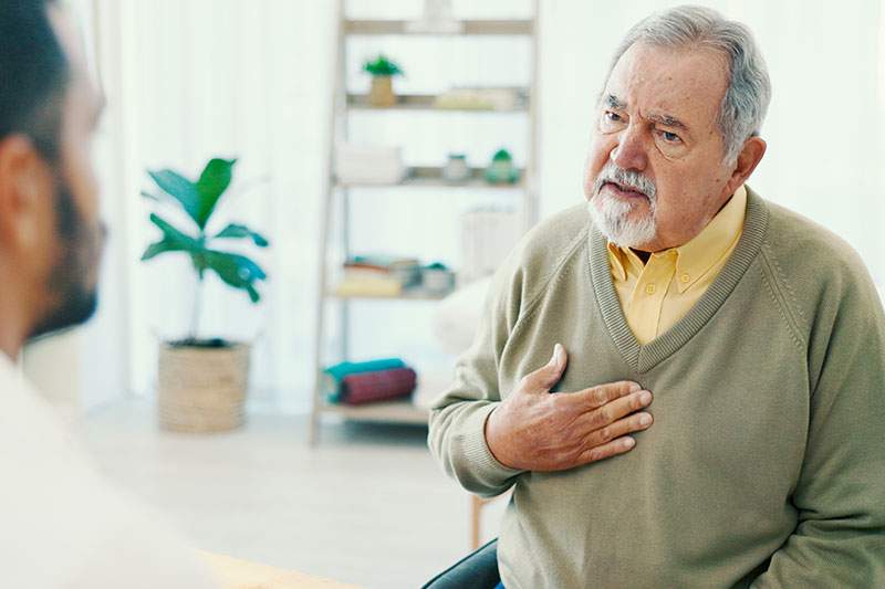 An older man sitting with his hand over his heart.
