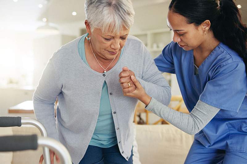 A nurse assists an elderly woman using a walker