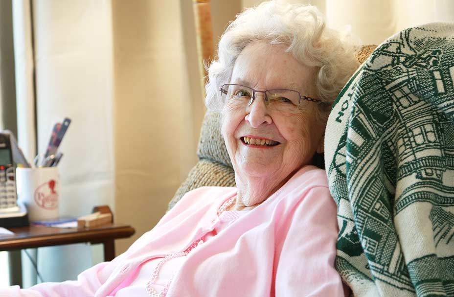 A senior sits in a chair in her living room and smiles