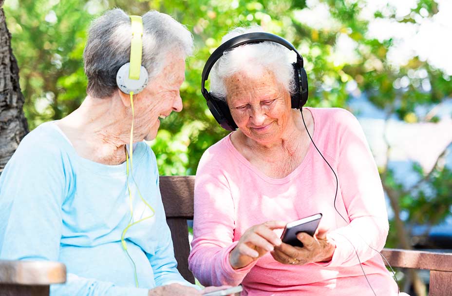 Two seniors look at a phone together. Both are wearing headsets