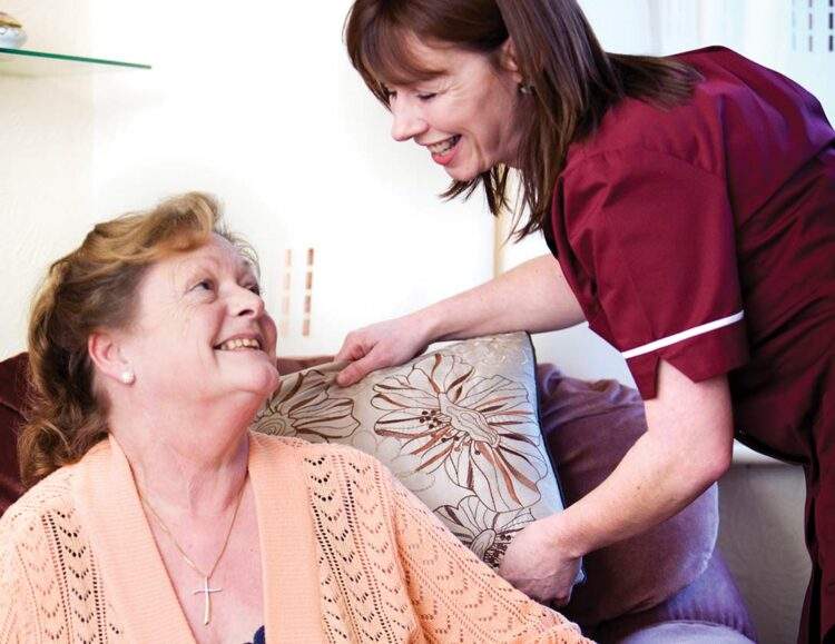 A caregiver leans down to speak to a client