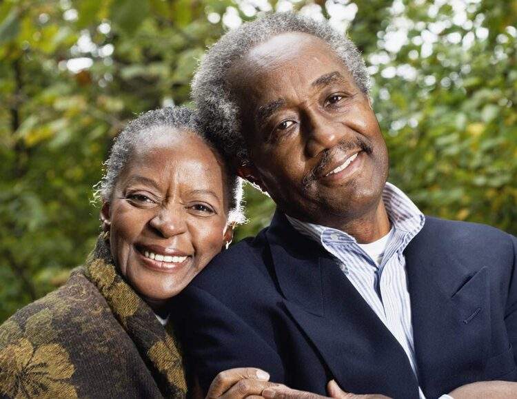 A smiling senior couple stands side-by-side and smiles