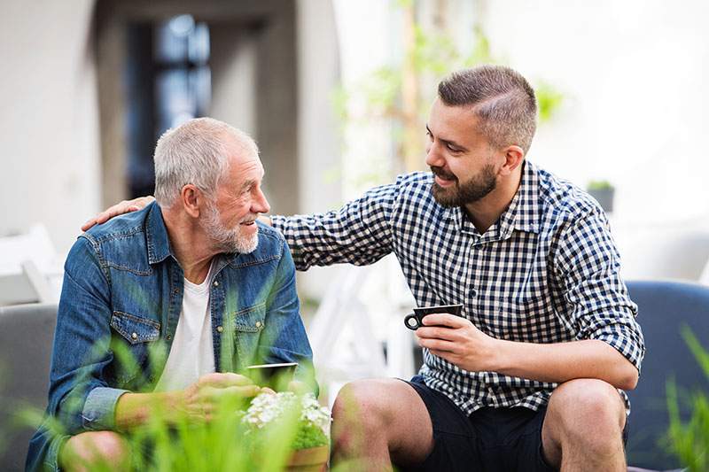 younger man with his arm over an elderly man, both sitting