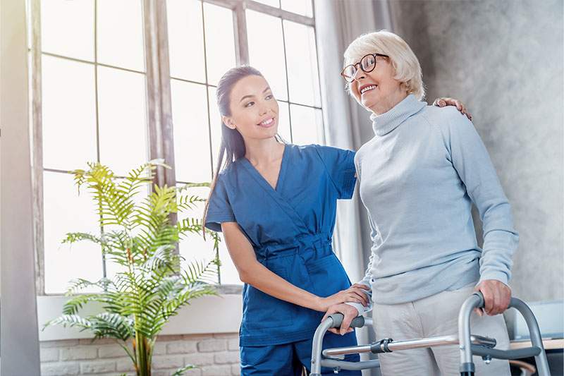 A older woman using a walker stands beside a younger woman